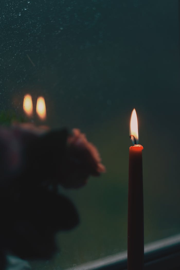 A serene lit candle reflects on a window, evoking warmth and tranquility.