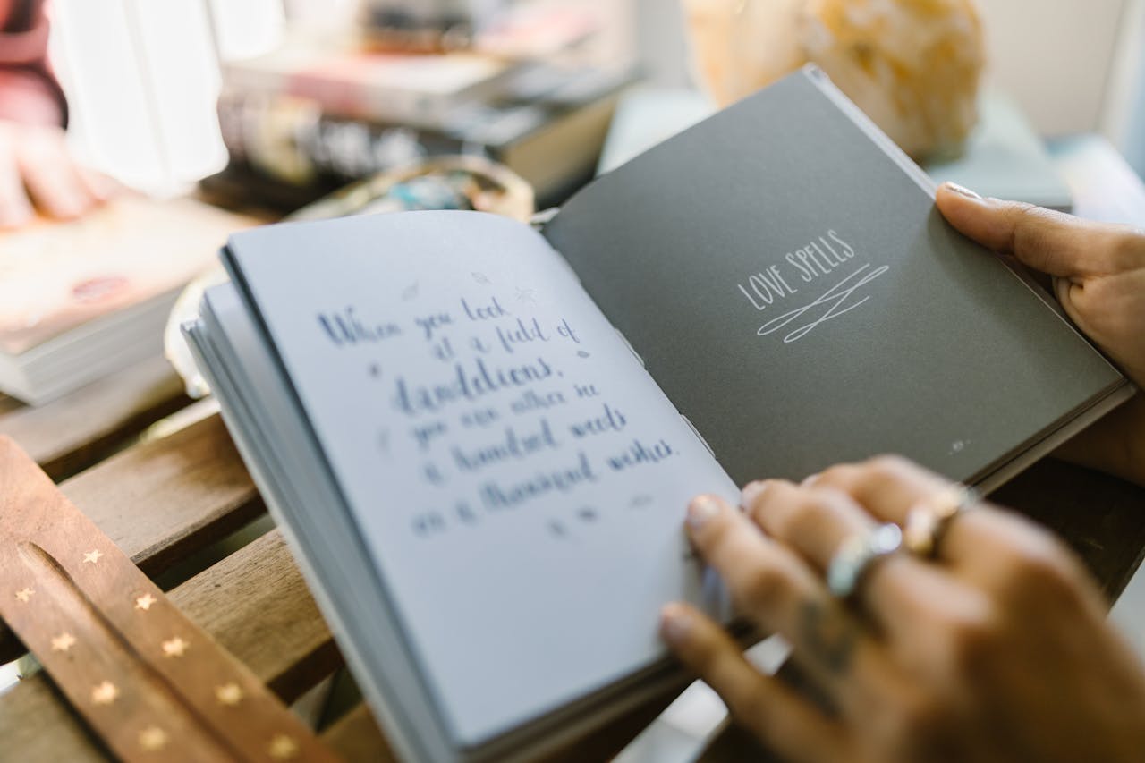 Close-up of hands holding an open book with text about love spells on a wooden table.